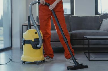 pexels photo 6195273 6195273 A professional cleaner in red coveralls vacuums a contemporary living room with a yellow vacuum cleaner.